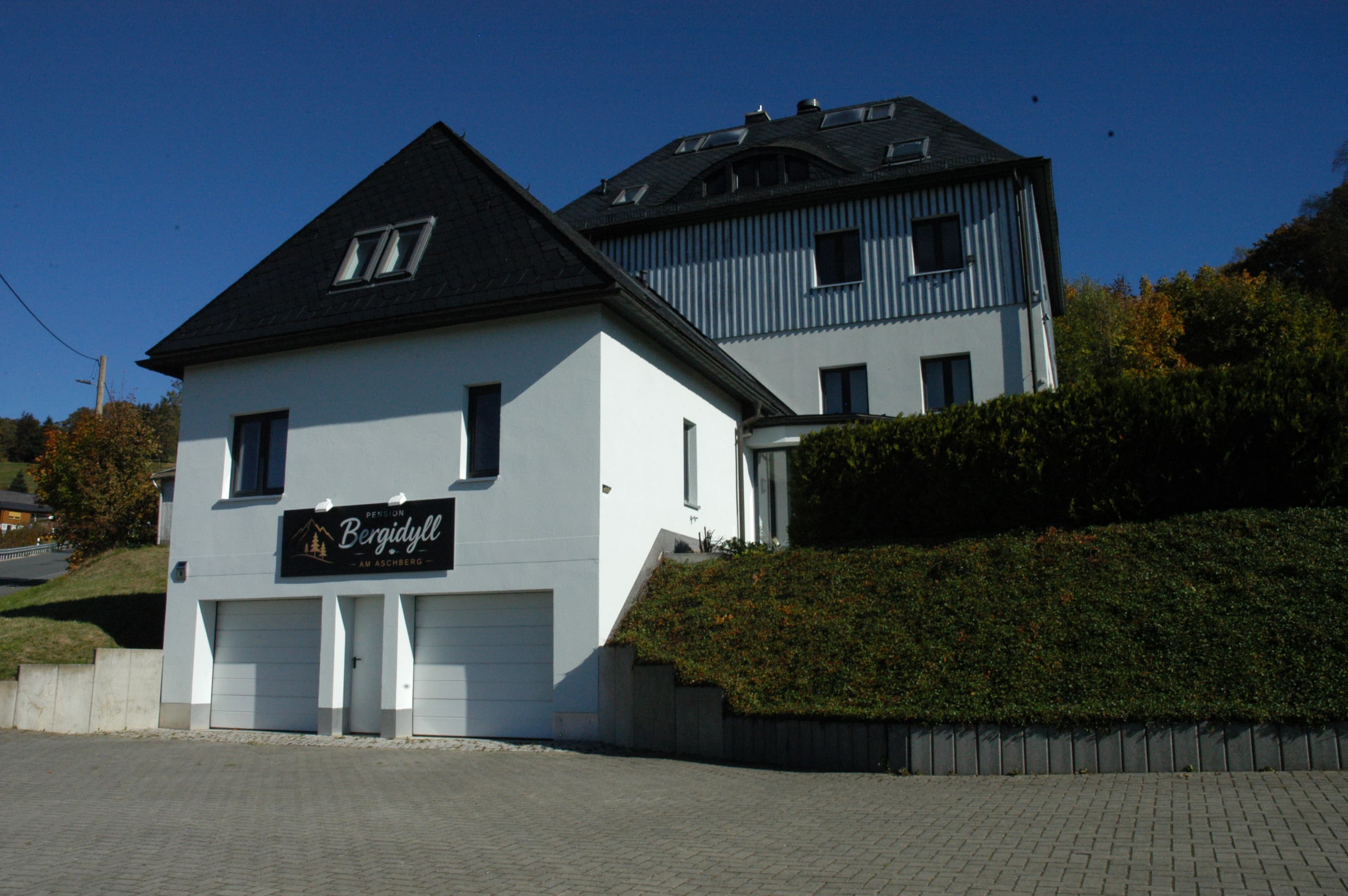 Pension Bergidyll mit weißer Fassade, dunklem Dach und Pensionsschild über den Garagen
