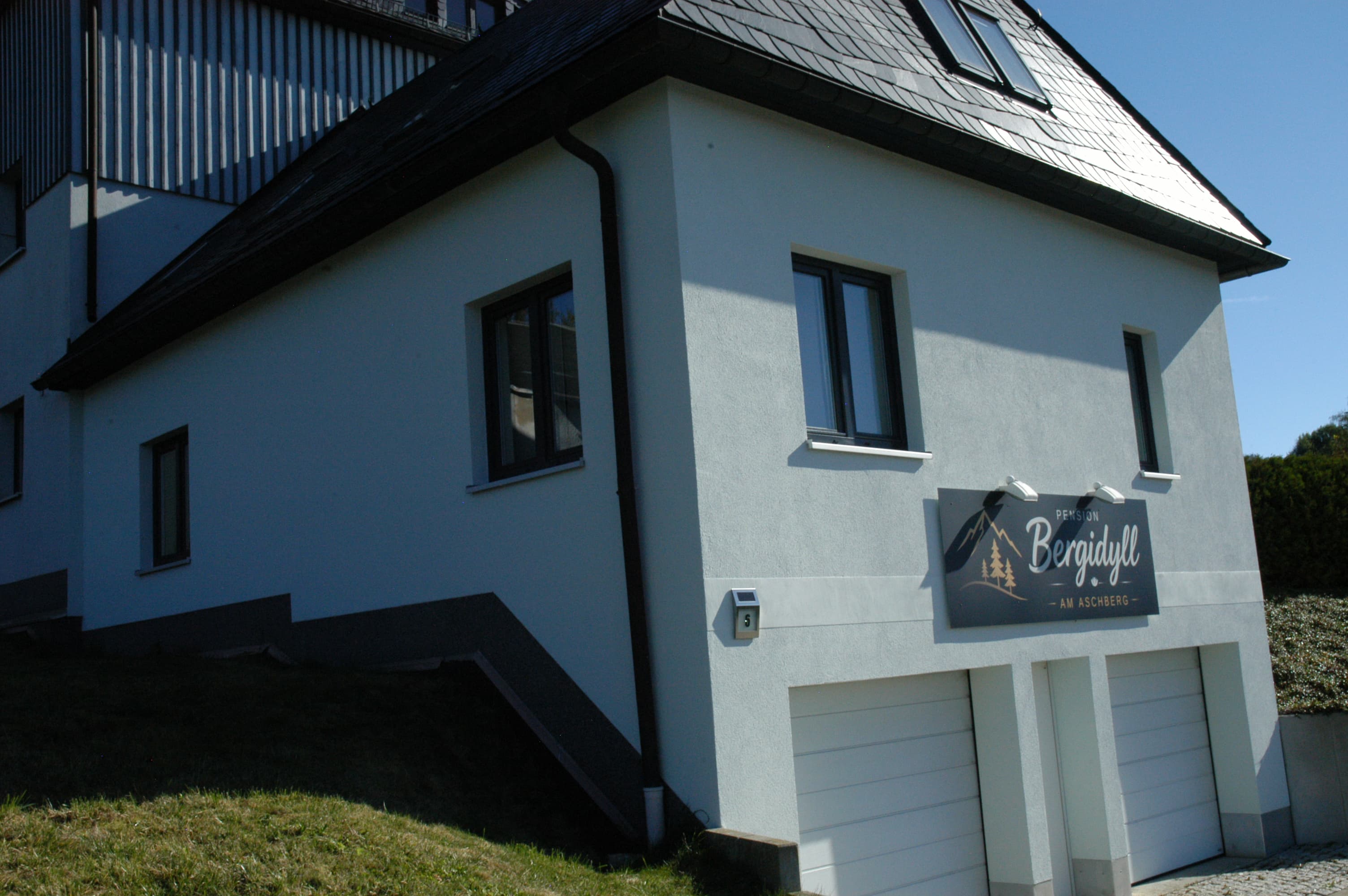 Schild „Pension Bergidyll am Aschberg“ an der weißen Hausfassade über den Garagen